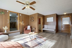 A room with a ceiling fan, wooden walls, a round coffee table, a bench, and a door with a sign.