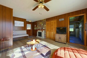 A cozy living room with a wooden ceiling fan, a stone fireplace, a television, and a bench.