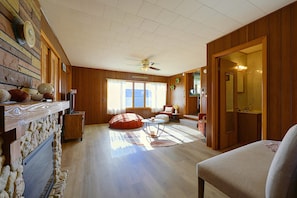 A spacious living room with a fireplace, wooden walls, and a large window.