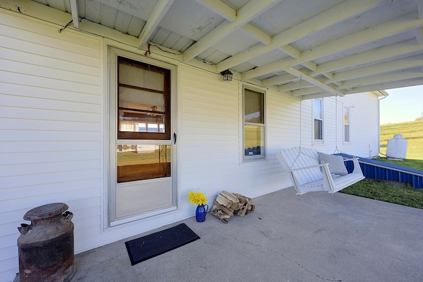 A covered porch with a white exterior, a wooden door, and a window.
