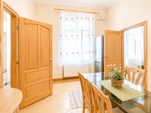 Une pièce avec des portes en bois, une table en verre, une chaise, une petite table avec une plante et une fenêtre avec un rideau.