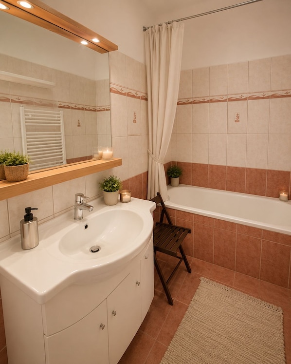 Une salle de bain avec un lavabo blanc, un miroir, un porte-serviettes, un rideau de douche et une baignoire.