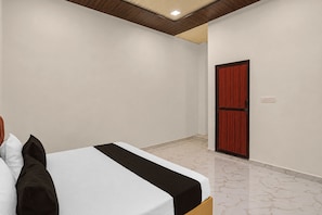 A bedroom with a bed, a wooden door, and a tiled floor. - Hotel O Ganeshpur Inn (Lucknow)