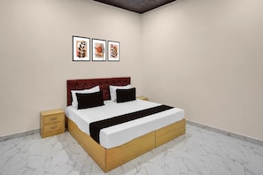 Un dormitorio con cama, mesita de noche, cajón de madera y tres cuadros enmarcados en la pared.