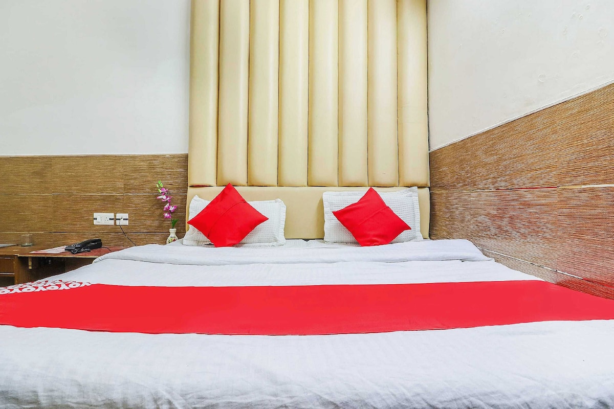 Habitació d'hotel amb un llit, una taula de nit, un vas amb flors i un panell de capçal de fusta.