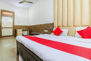 Habitació d'hotel amb llit, escriptori, cadira, armari i ventilador de sostre.