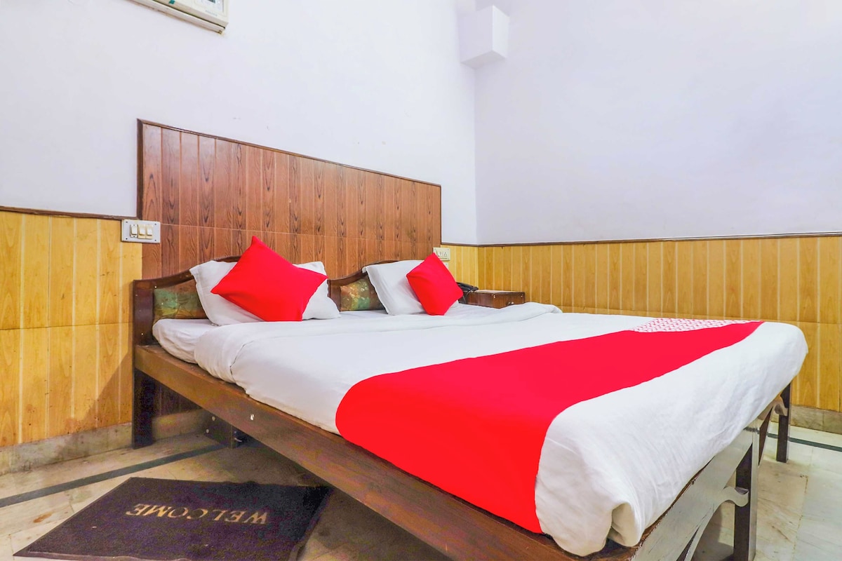 A double bed with a wooden headboard, white bedding, and red pillows in a room with wooden paneling on the walls.