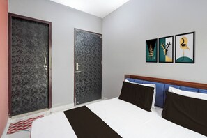 Una habitació d'hotel amb un llit, dues portes i tres quadres emmarcats a la paret.