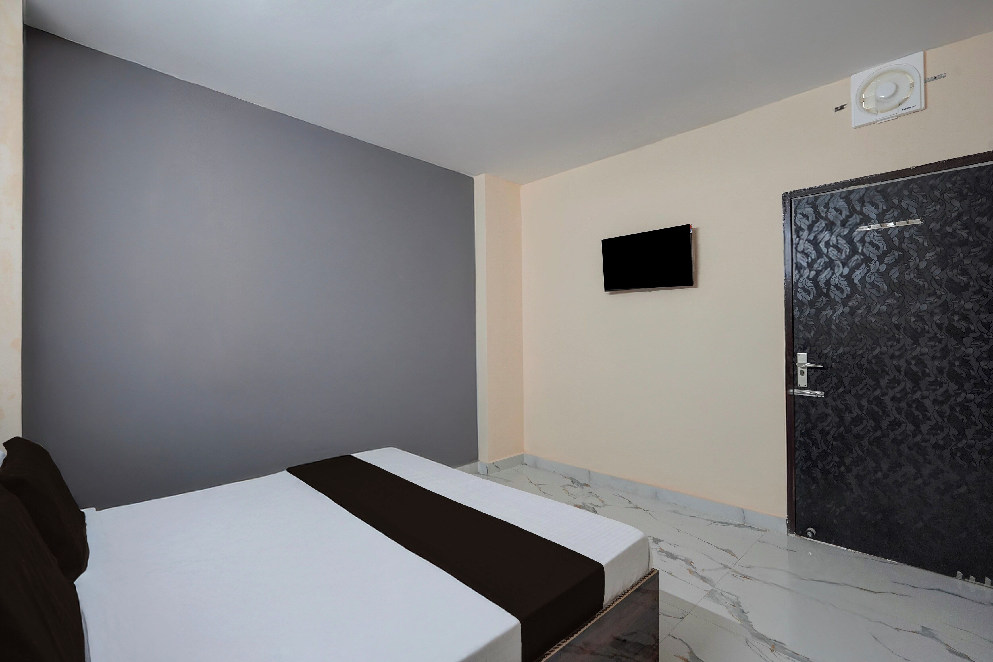 Habitación de hotel con una cama, un televisor de pantalla plana montado en la pared y una puerta con diseño decorativo.