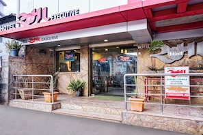 A hotel entrance with a red and white facade, a glass door, and potted plants. - Hotel O Rama Executive (Mahabaleshwar)