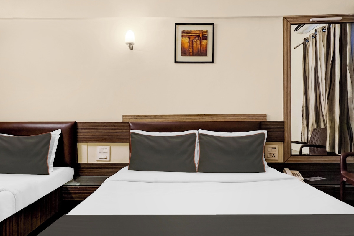 Een hotelkamer met twee bedden, een nachtkastje, een lamp, een schilderij en een raam met gordijnen.
