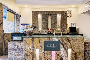 A reception desk with a marble counter, a sign for the Collection, and a framed photo on the wall. - Hotel O Rama Executive (Mahabaleshwar)