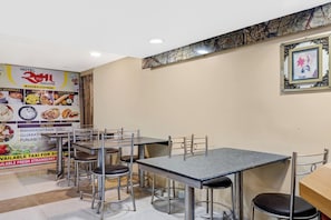 A restaurant interior with multiple tables and chairs, a menu board on the wall, and a framed picture on the wall. - Hotel O Rama Executive (Mahabaleshwar)