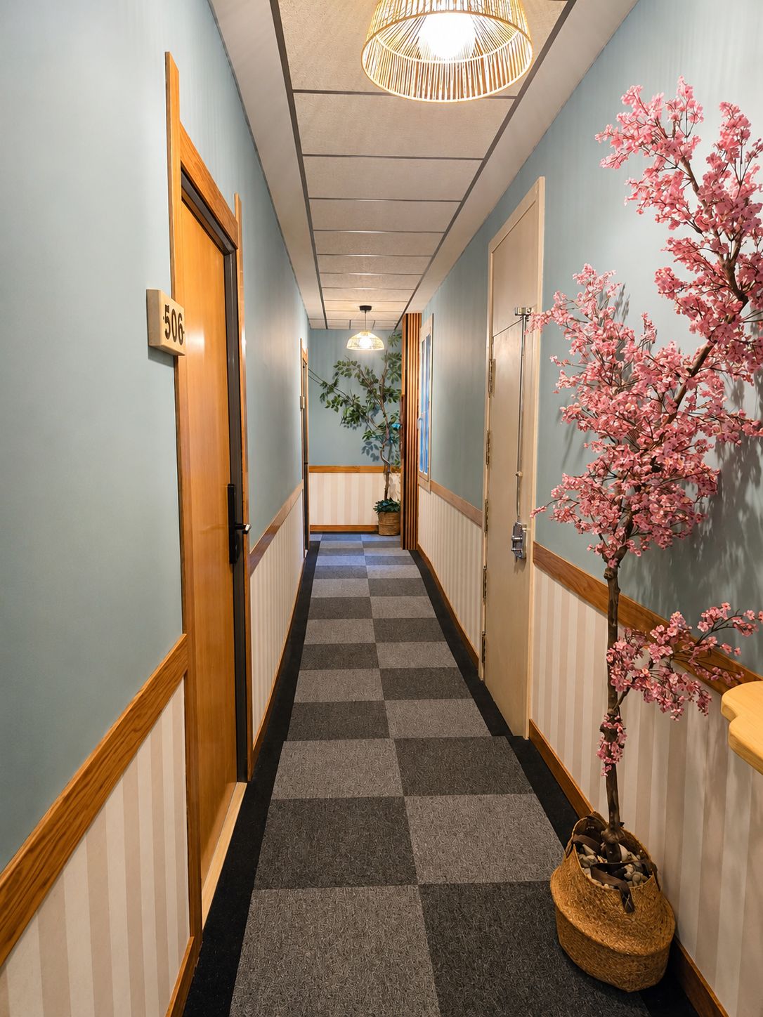 Un pasillo de hotel con alfombra a cuadros, puertas de madera y un árbol de cerezo.