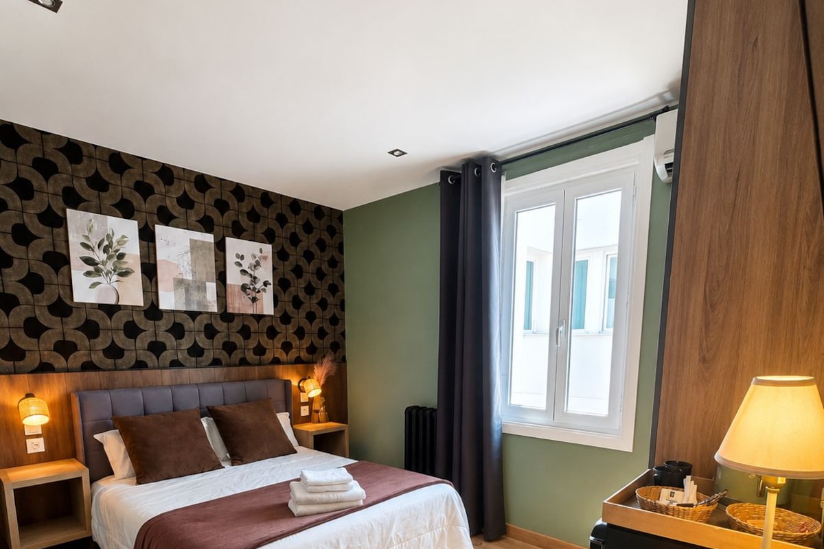 A hotel room with a bed, bedside tables, a desk, and a lamp.