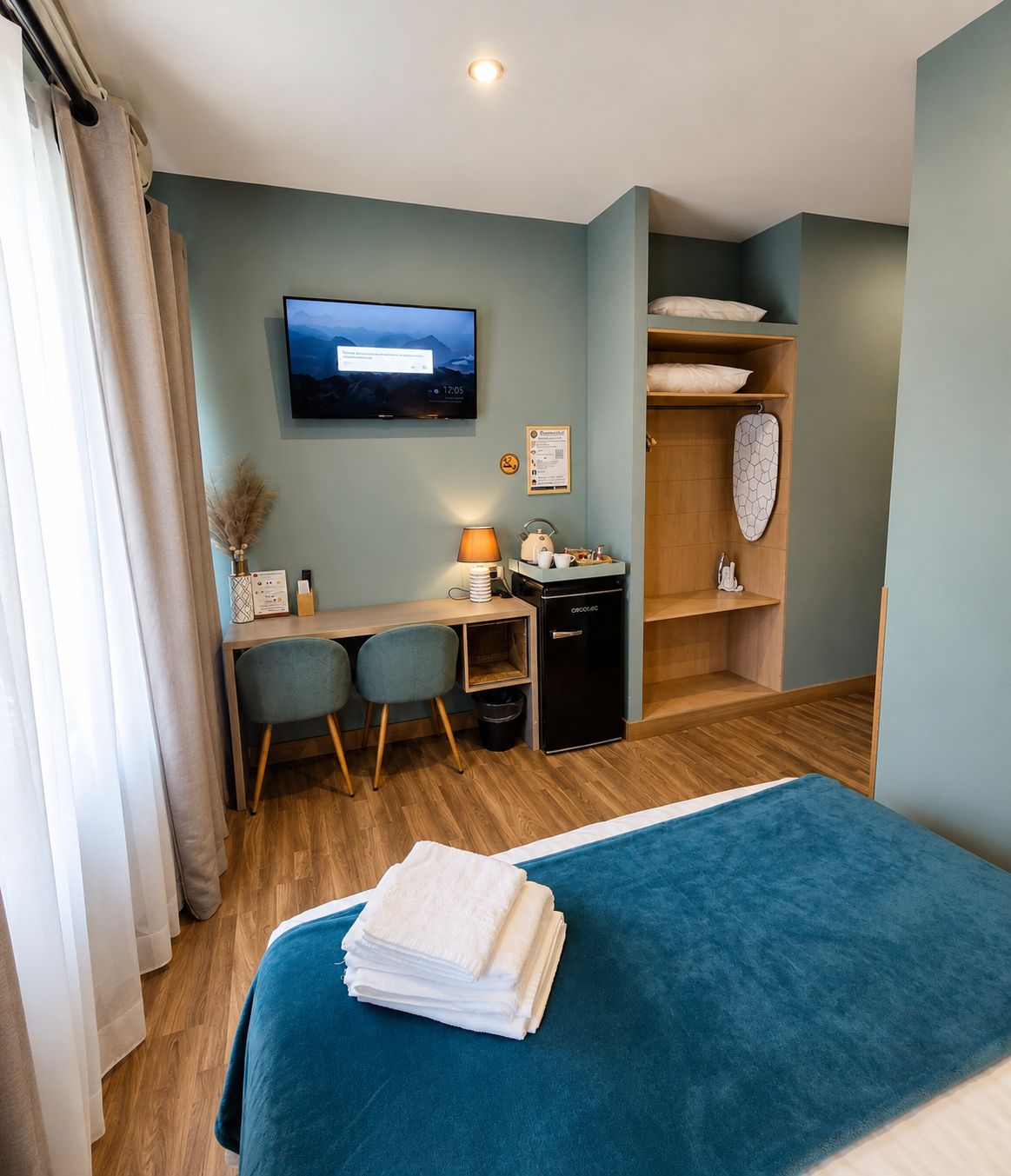 Una habitación de hotel con una cama, un escritorio con computadora, un televisor y un armario.