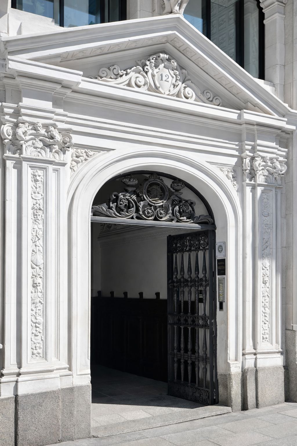Una entrada blanca y ornamentada con un portón negro, que presenta intrincados grabados y un diseño clásico.
