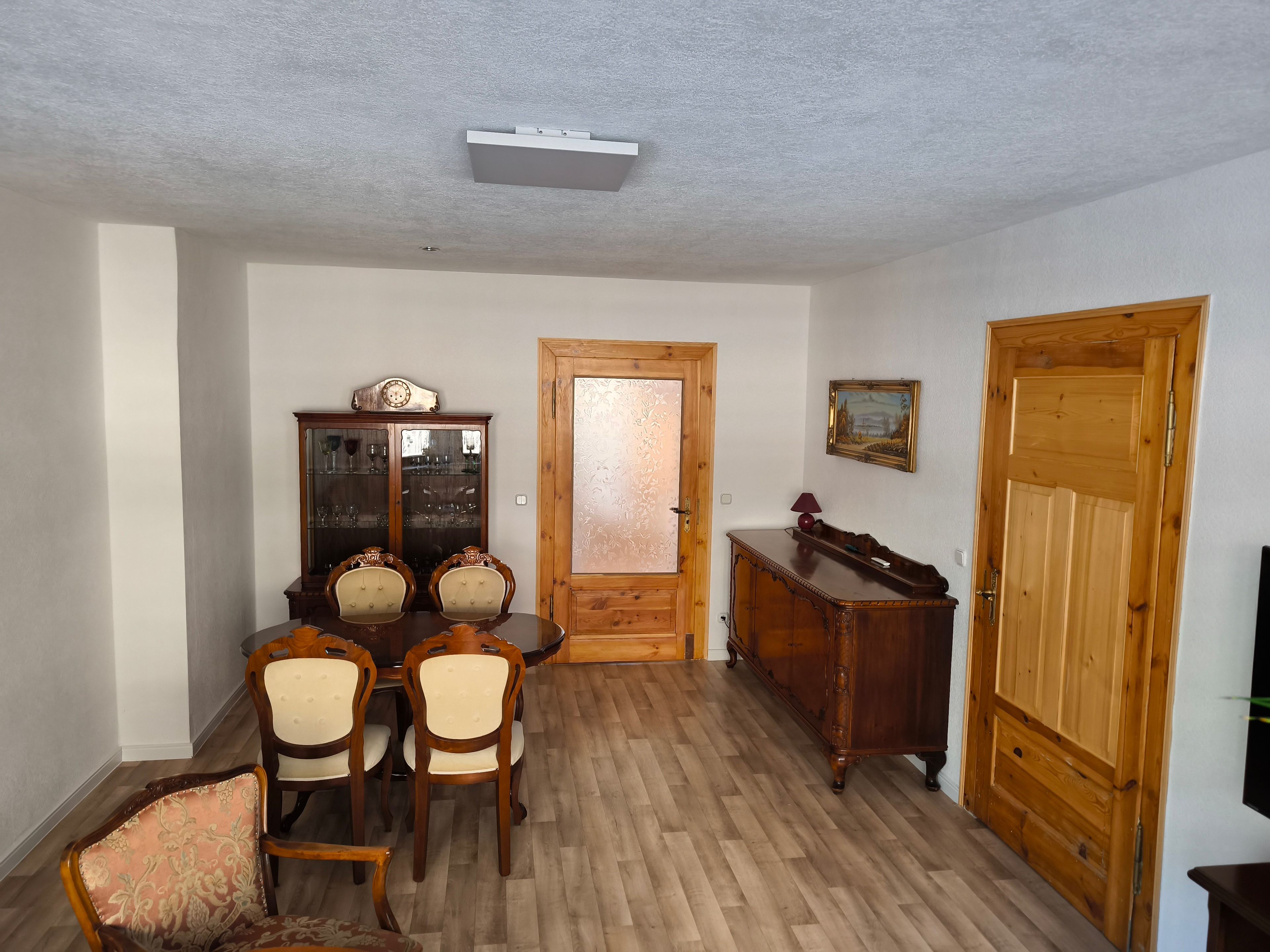 Ein Esszimmer mit Holztisch und -stühlen, einem Holzschrank, einer Holztür und einem gerahmten Bild an der Wand.