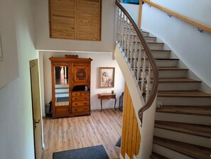 Eine Treppe mit Holzsitzstufen und einem weißen Geländer, die zu einer Zwischenebene mit einem Holzkasten und einem gerahmten Bild führt.