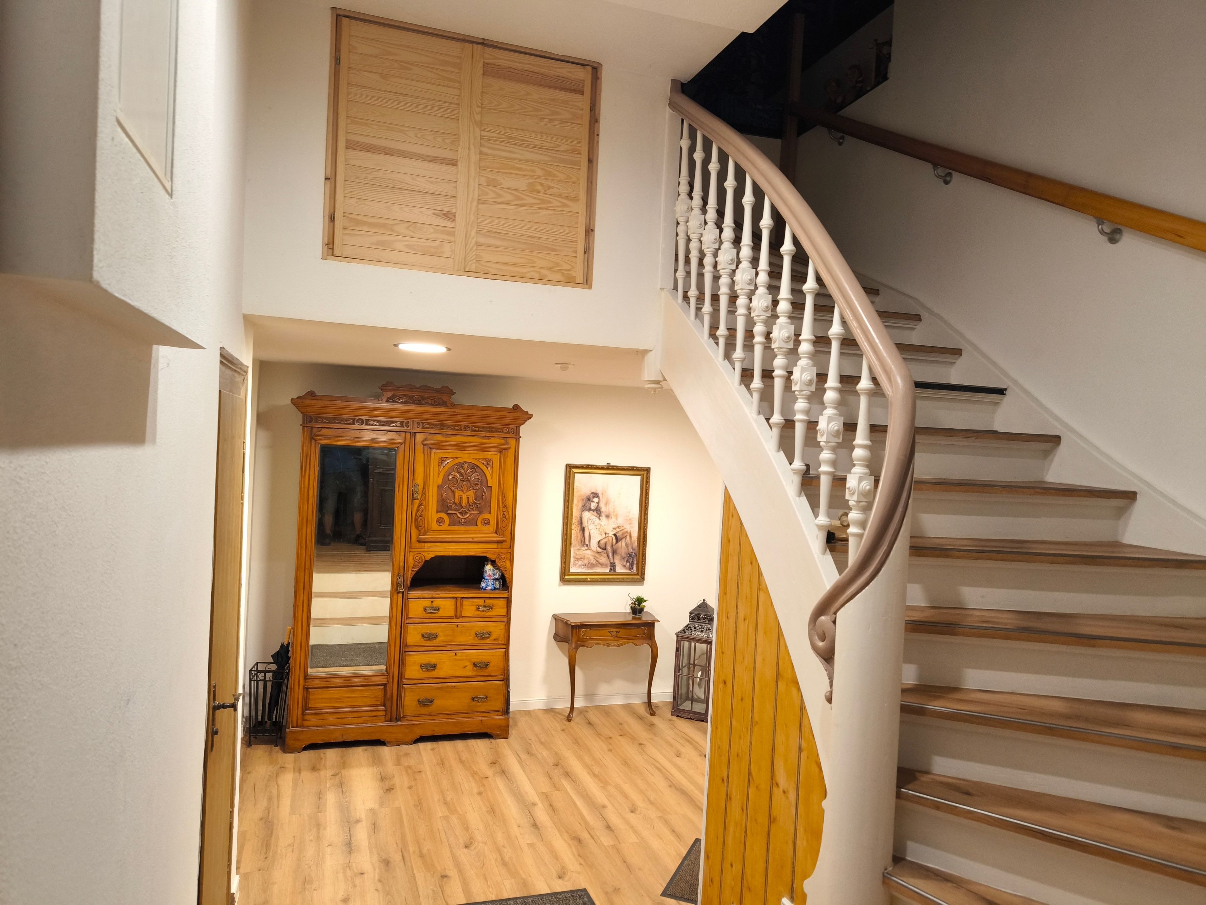 A staircase with a wooden handrail and white balusters, leading to a landing with a wooden cabinet and a framed picture on the wall.