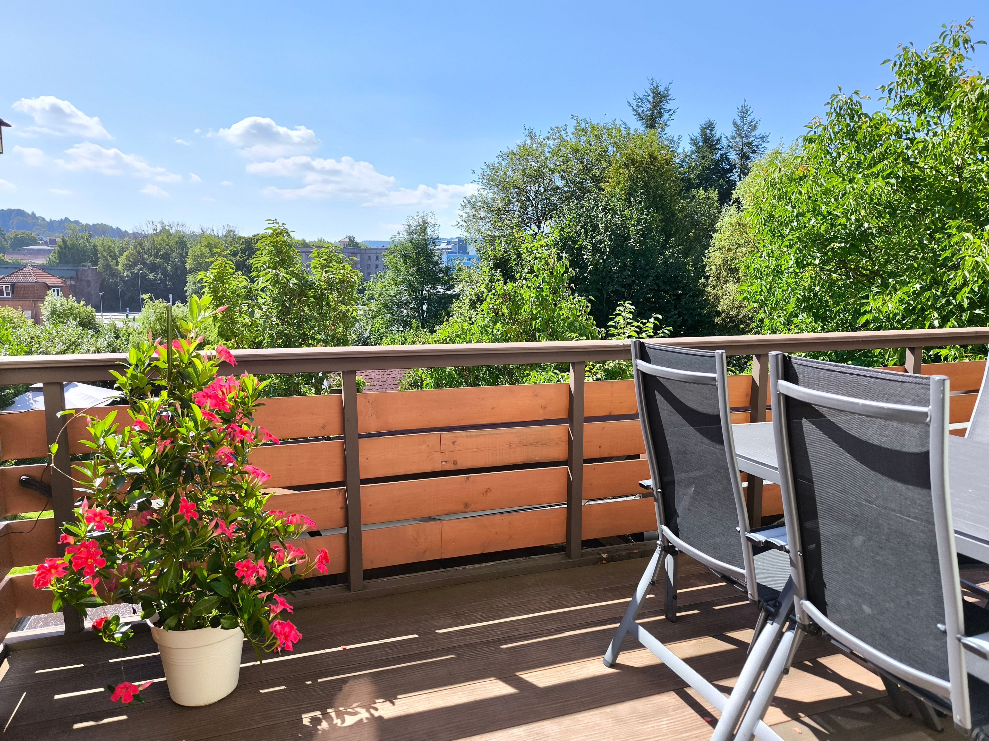 Um deck de madeira com um vaso de planta e duas cadeiras.