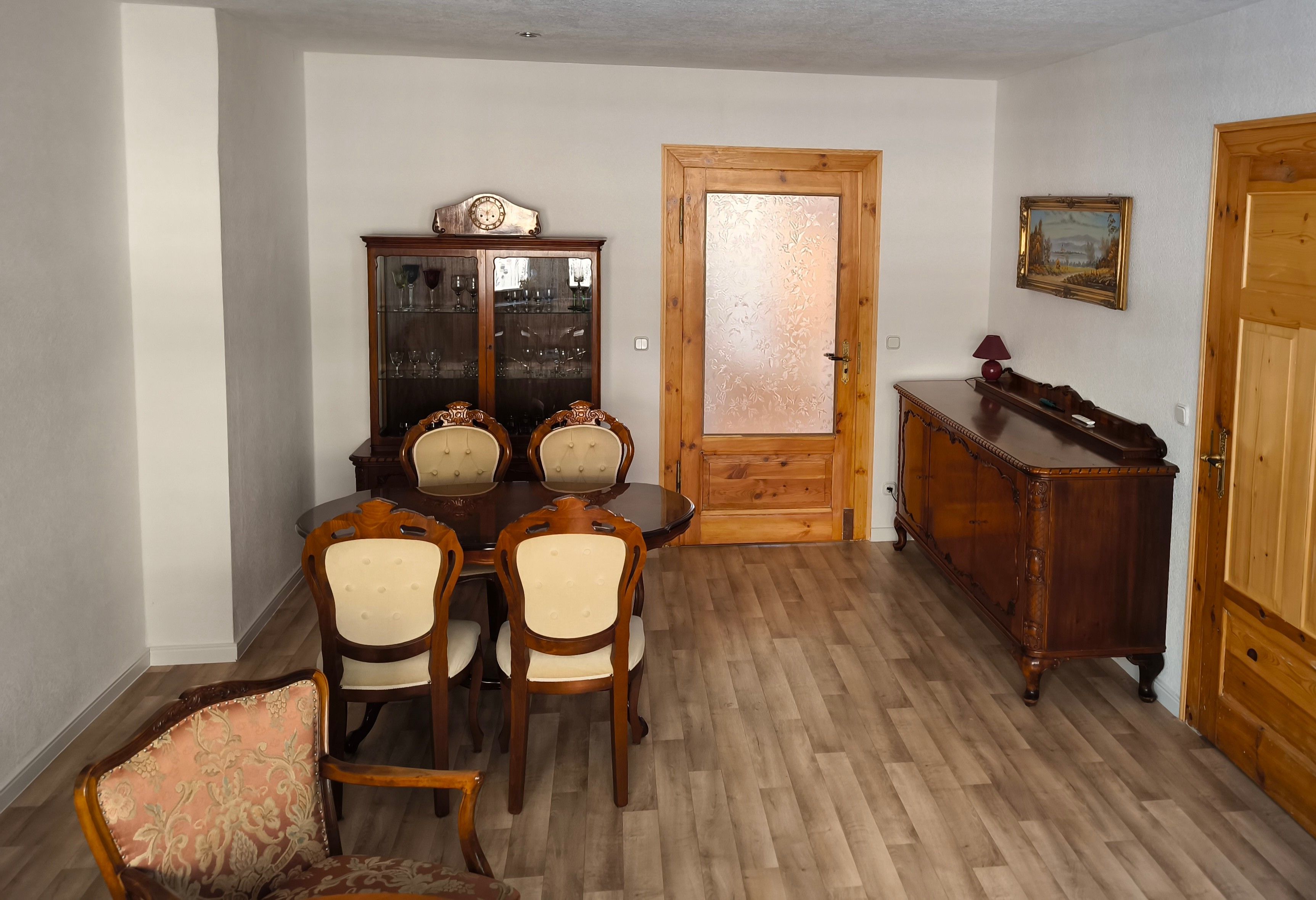 Uma área de refeições com mesa e cadeiras de madeira, um armário com portas de vidro e uma porta de madeira com painel de vidro jateado.