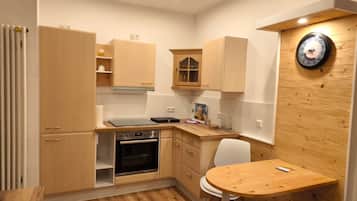 Eine kleine Küche mit Holzausstattung, einem eingebauten Backofen, einem Esstisch mit einem Stuhl und einer Wanduhr.