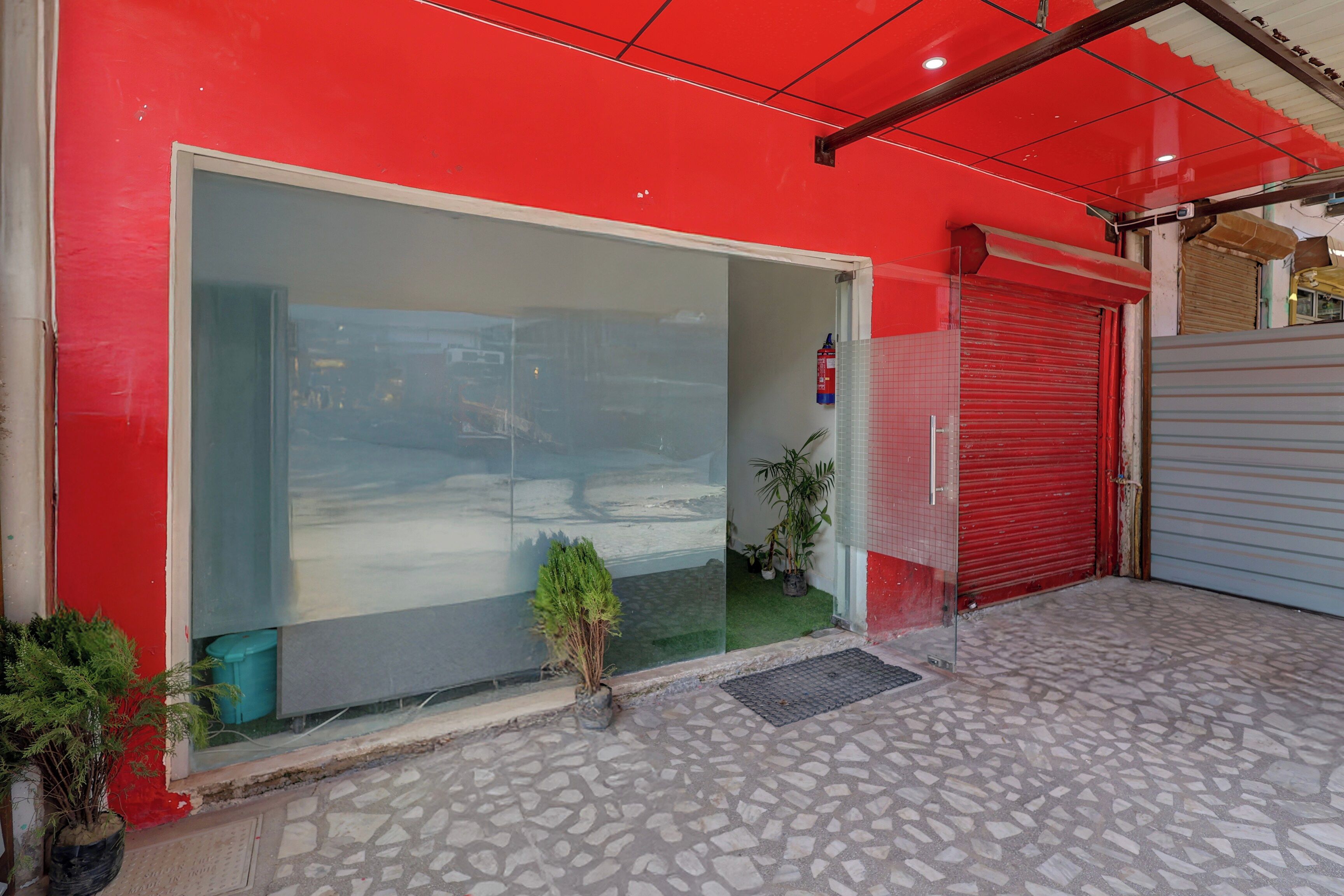 Un edificio con fachada roja, un amplio ventanal y un persiano rojo cerrado.