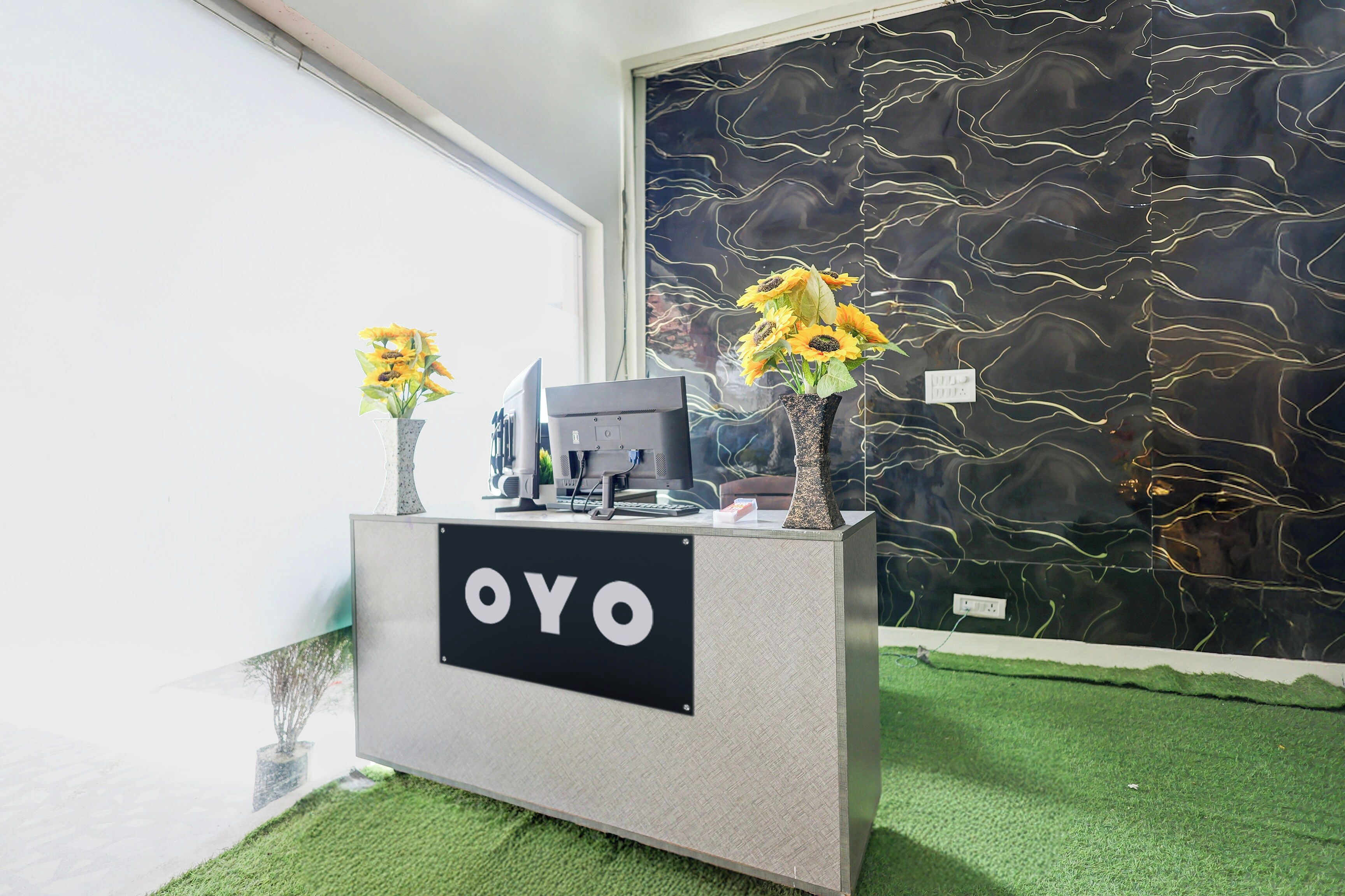 A reception desk with a sign reading 'OYO,' a computer, and two vases with sunflowers.