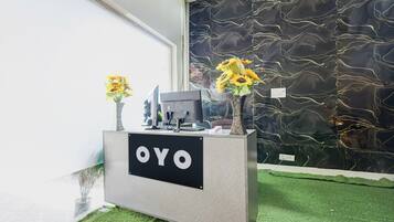 Una mesa de recepción con un letrero que dice 'OYO', una computadora y dos jarrones con girasoles.