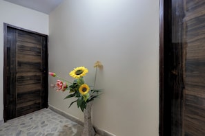 A hallway with a tiled floor, a wall-mounted vase with flowers, and wooden doors. - Hotel O New Star Hotel (Gurugram)