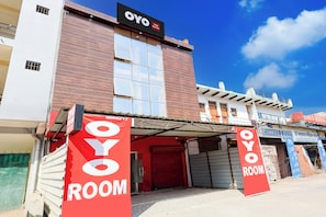 Un hotel con un llamativo letrero 'OYO ROOM', fachada moderna y un cielo azul despejado.