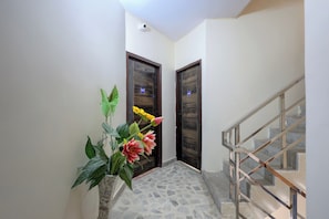 A hallway with a staircase, a potted plant with flowers, and two wooden doors. - Hotel O New Star Hotel (Gurugram)