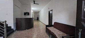Un pasillo con una recepción, un sofá, un ventilador de techo y una escalera.