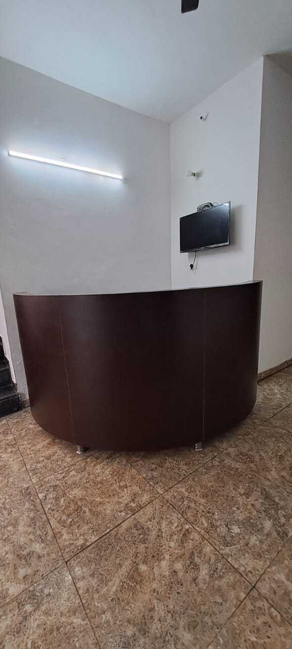 A reception desk with a flat-screen TV mounted on the wall, a ceiling light fixture, and a tiled floor.
