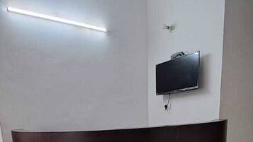 Una recepción con un televisor de pantalla plana en la pared, una lámpara en el techo y piso de baldosas.