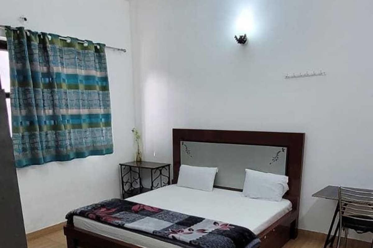 Un dormitorio con cama, ventilador de techo, ventana con cortinas y una pequeña mesa con sillas.