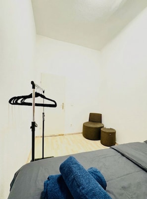 A room with a bed, a hanging clothes rack, and two round stools. - The Vienna Pause Private Room for Two (Wien)