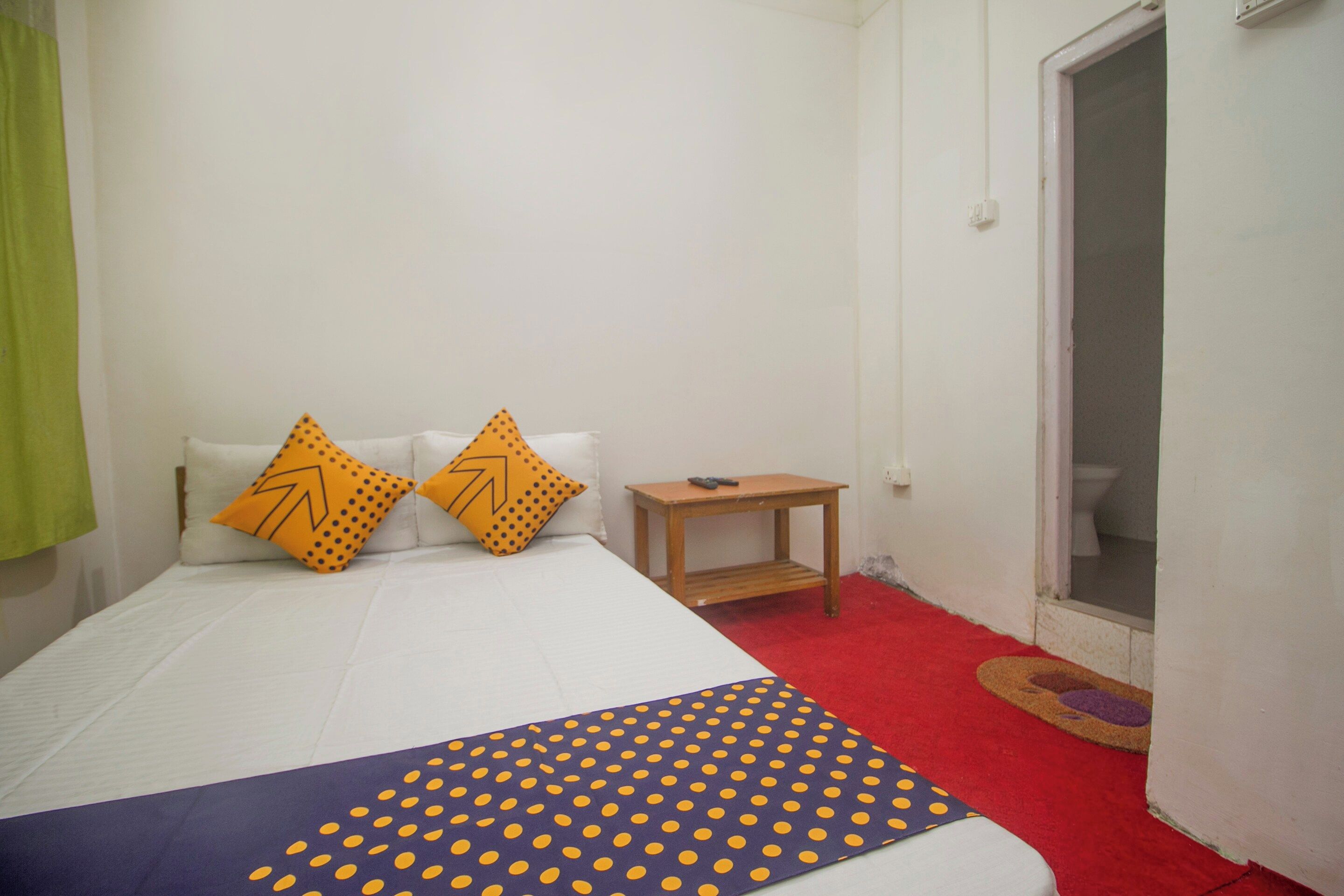 A bedroom with a bed, two pillows, a small wooden nightstand, and a red carpet.