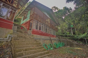 Ein Gebäude mit einer Treppe, die zu einer roten und grünen Struktur führt, umgeben von Grünpflanzen.