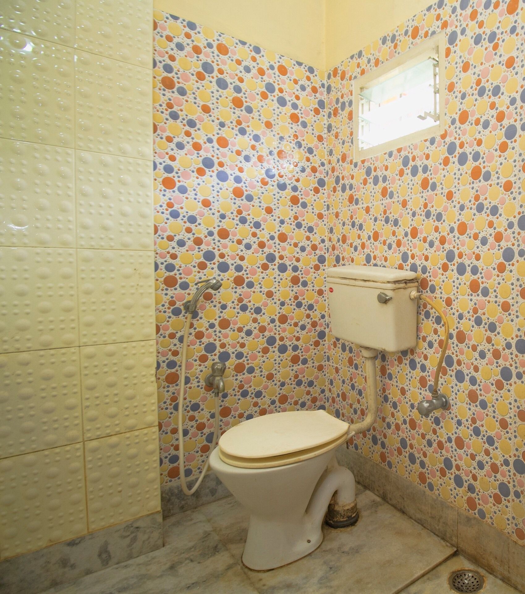 A bathroom with a toilet, shower, and tiled walls with a polka dot pattern.