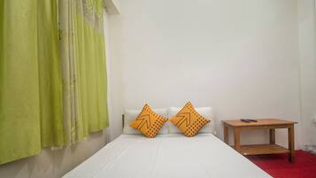 A single bed with white bedding and two orange pillows with a leaf pattern, a green curtain, and a small wooden nightstand with a remote control.