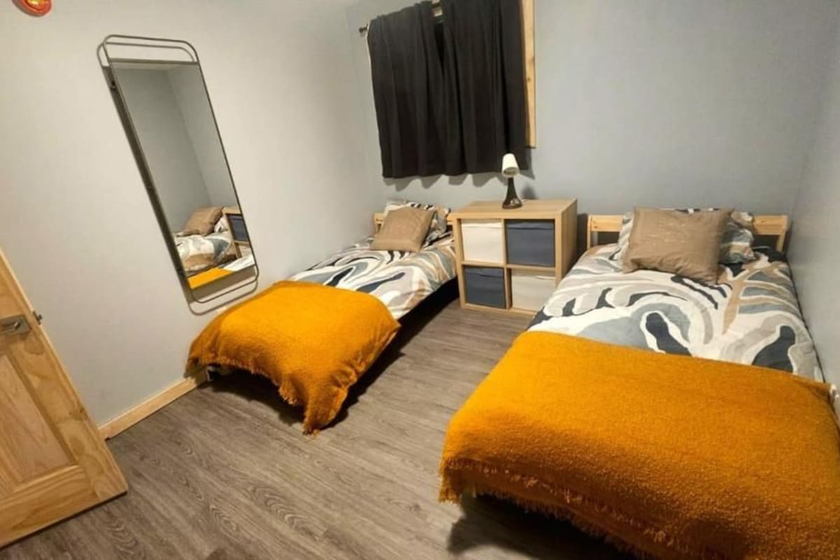 Een slaapkamer met twee bedden, een nachtkastje, een spiegel en een deur.