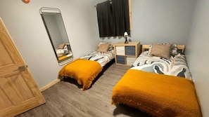Een slaapkamer met twee bedden, een nachtkastje, een spiegel en een deur.