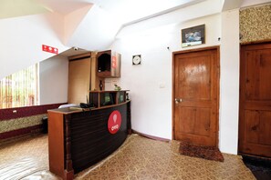A reception desk with a clock, a door, and a patterned floor. - Hotel O Manali Meadows Home Stay (Manali)