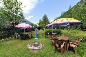 Un espace extérieur aménagé avec des tables et des chaises, entouré de verdure et offrant une vue sur les montagnes en arrière-plan.