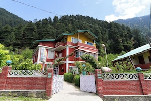 A two-story building with a red and yellow facade, a gated entrance, and a mountainous backdrop. - Hotel O Manali Meadows Home Stay (Manali)
