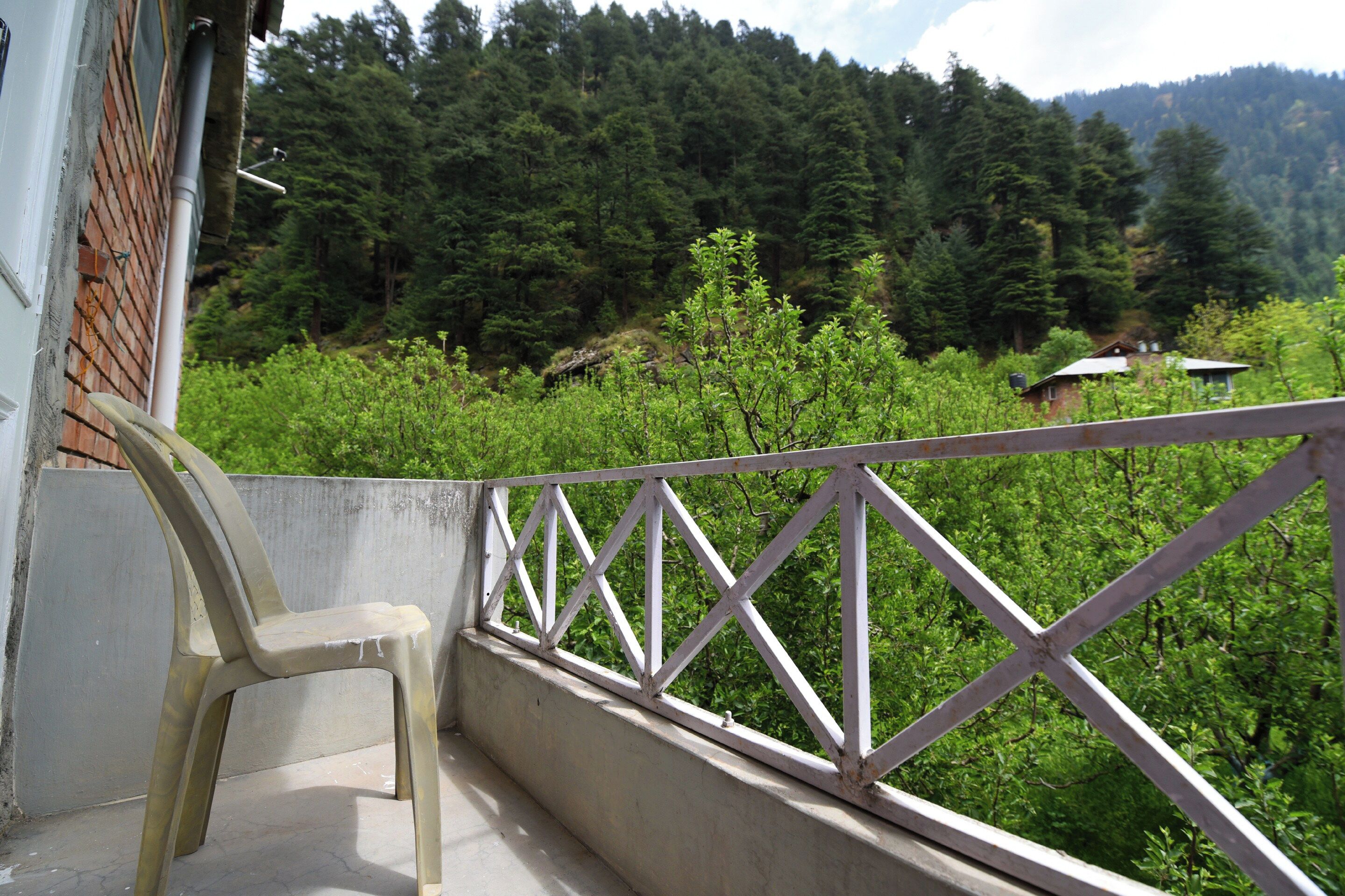 A balcony with a concrete floor, a white railing, and a plastic chair.