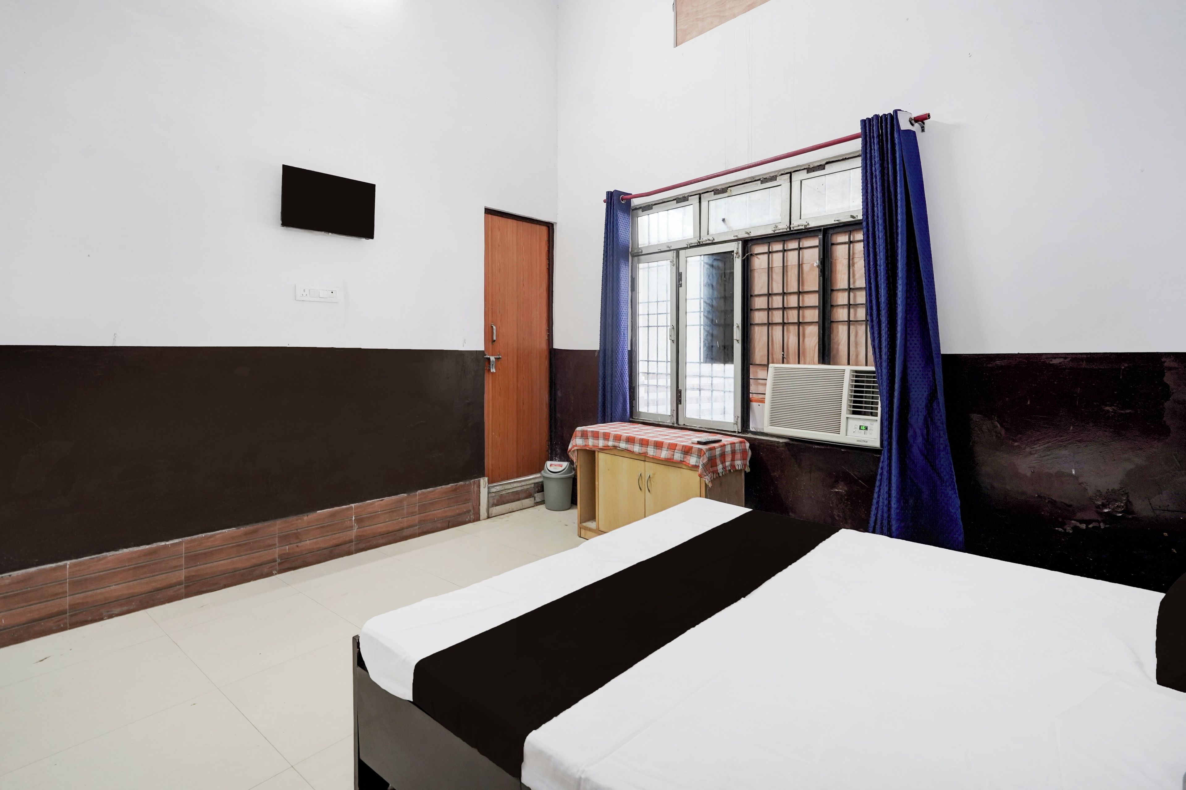 Habitación de hotel con una cama, un ventanal con cortinas, una mesita con mantel y un calentador de pared.