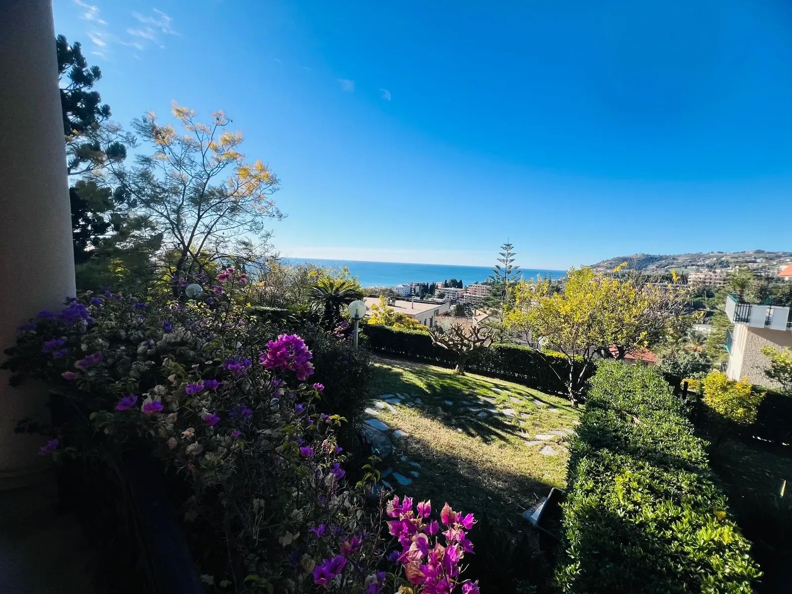 A garden with a view of the sea and buildings in the distance.
